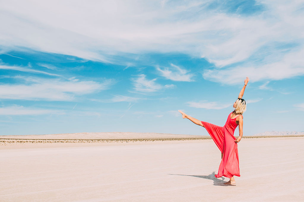 tanzende Frau mit rotem Kleid in der wüste und strahlend blauem Himmel
