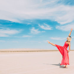 tanzende Frau mit rotem Kleid in der wüste und strahlend blauem Himmel