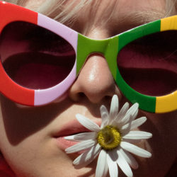 close-up Frau mit bunter Sonnenbrille und Blume im Mund