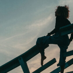 Frau sitzt in Sonnenuntergangs-Stimmung auf einem Geländer