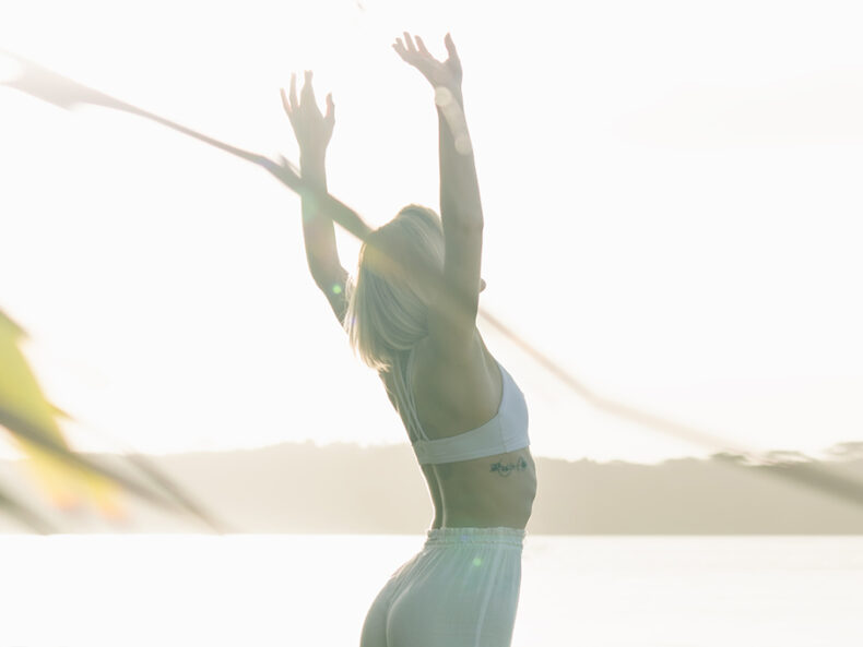Frau im Morgenlicht an einem See in einer Yoga Asana