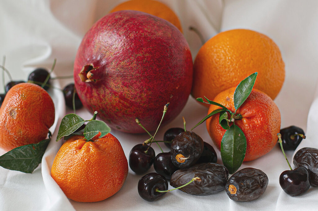 Stillleben eines Granatapfels mit Mandarinen, Kirschen und Datteln